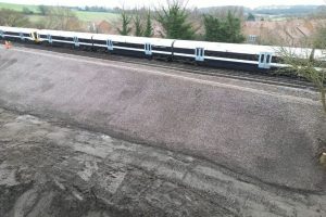A photo of freshly laid material forming an embankment up to a rail line with train carriages on it