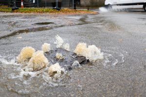 A stock photo of water gushing up out of a manhole cover on a street