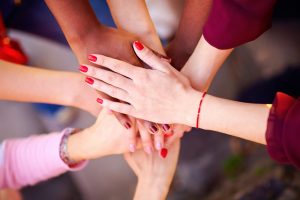 A stock image of a diverse set of hands on top of each other with red nail varnish on the hand at the top