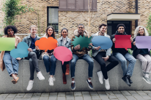 A group people sit on a wall holding colourful speech bubbles